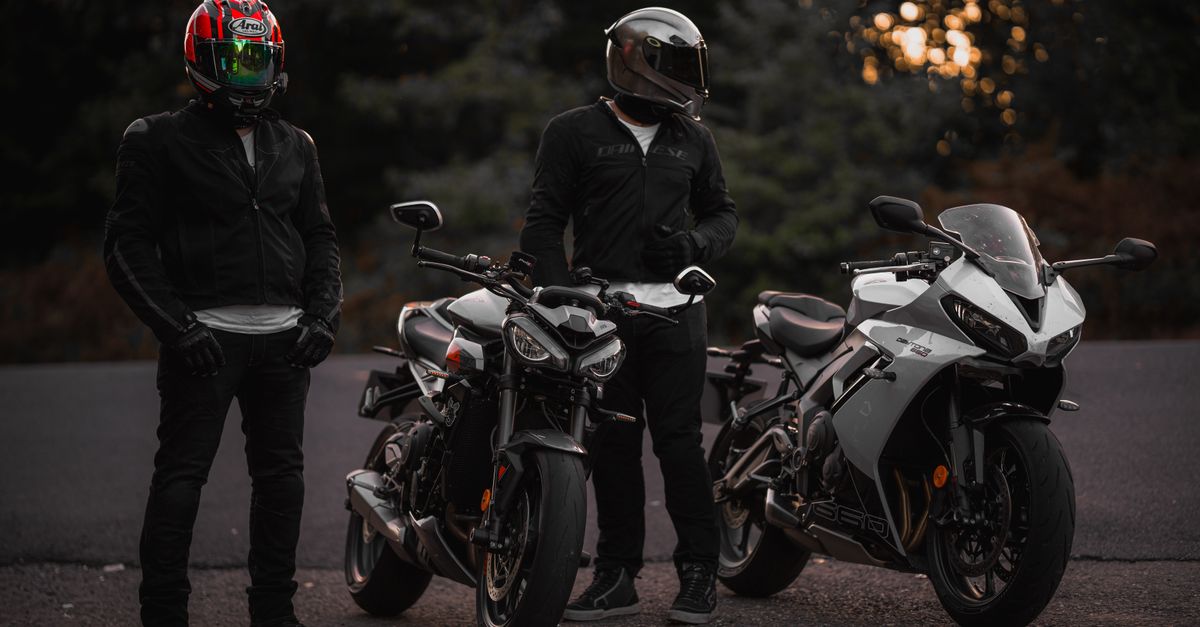 Two bikers with helmets standing beside their sport motorcycles during twilight on a road.